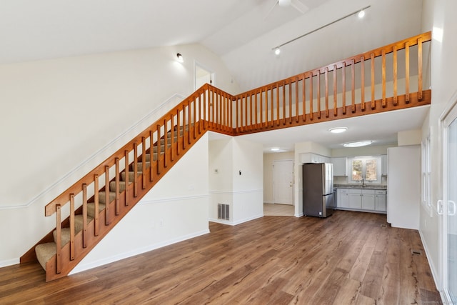 unfurnished living room with high vaulted ceiling, sink, hardwood / wood-style floors, and rail lighting