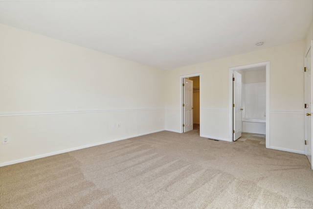 unfurnished bedroom with a spacious closet, light colored carpet, ensuite bath, and a closet