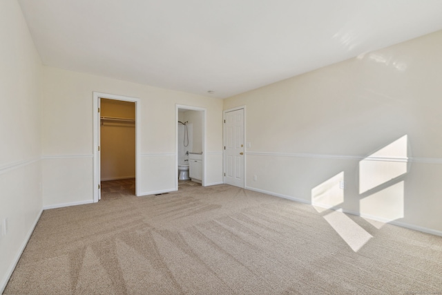 unfurnished bedroom featuring ensuite bathroom, a walk in closet, and light carpet