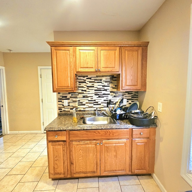 kitchen featuring light tile patterned flooring, dark stone counters, sink, and decorative backsplash