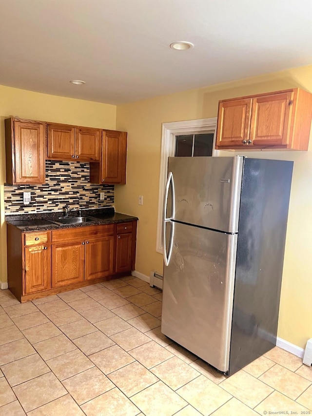 kitchen featuring sink, dark stone countertops, light tile patterned floors, stainless steel fridge, and decorative backsplash