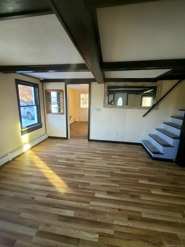 unfurnished living room featuring beamed ceiling, stairway, a textured ceiling, and wood finished floors