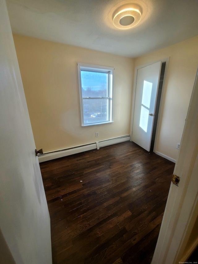 empty room featuring a baseboard heating unit and dark wood finished floors