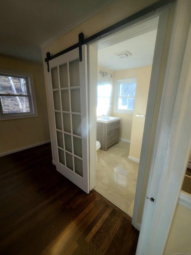 hallway featuring a barn door, visible vents, baseboards, wood finished floors, and a sink