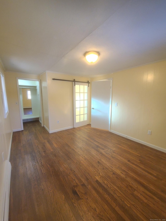 spare room featuring dark wood-style floors, baseboards, and a barn door