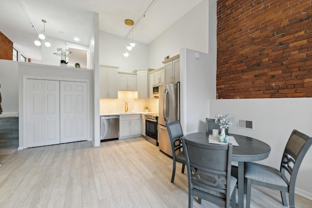 kitchen with stainless steel appliances, decorative light fixtures, sink, and light wood-type flooring