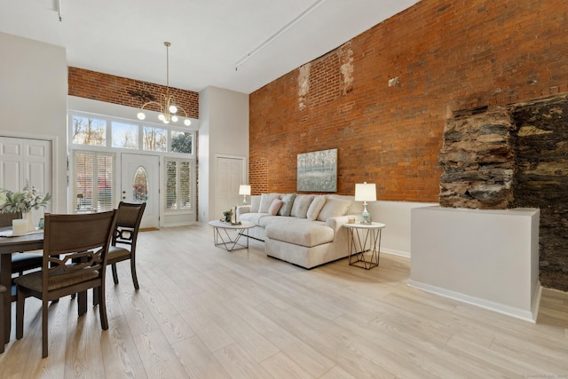 living room featuring a notable chandelier, a towering ceiling, light hardwood / wood-style floors, and brick wall