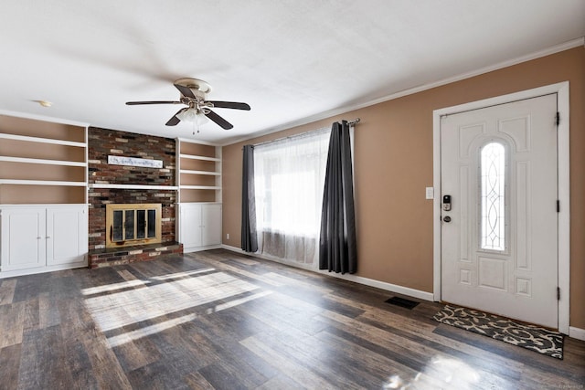 unfurnished living room featuring built in shelves, crown molding, dark hardwood / wood-style floors, ceiling fan, and a fireplace