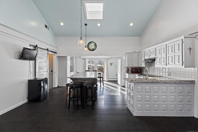 kitchen featuring white cabinetry, hanging light fixtures, kitchen peninsula, a barn door, and light stone countertops