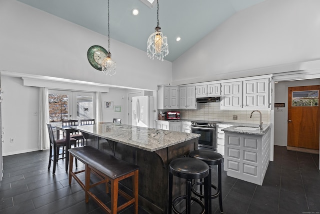 kitchen featuring a breakfast bar, hanging light fixtures, white refrigerator with ice dispenser, a kitchen island, and stainless steel range with electric cooktop