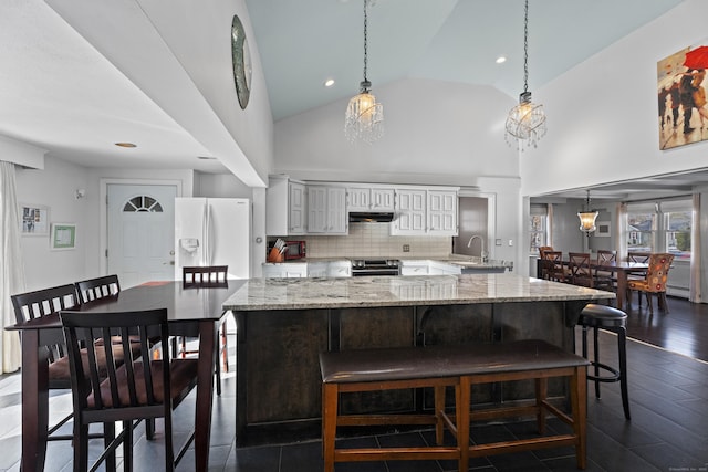 kitchen featuring a breakfast bar, light stone counters, white refrigerator with ice dispenser, stainless steel electric range oven, and decorative light fixtures