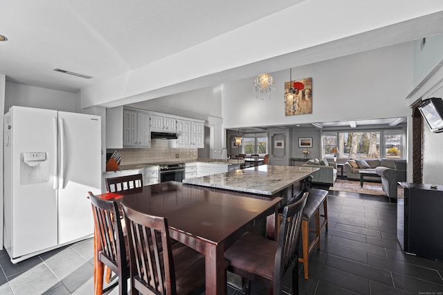 kitchen featuring a breakfast bar, white fridge with ice dispenser, stainless steel electric stove, decorative backsplash, and white cabinets