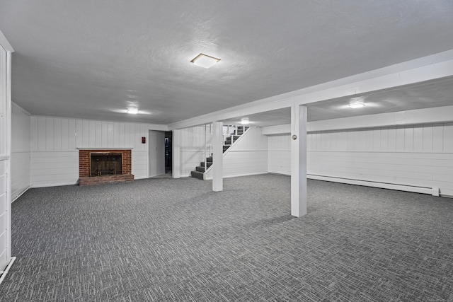 basement featuring dark colored carpet, a baseboard heating unit, a textured ceiling, and a fireplace