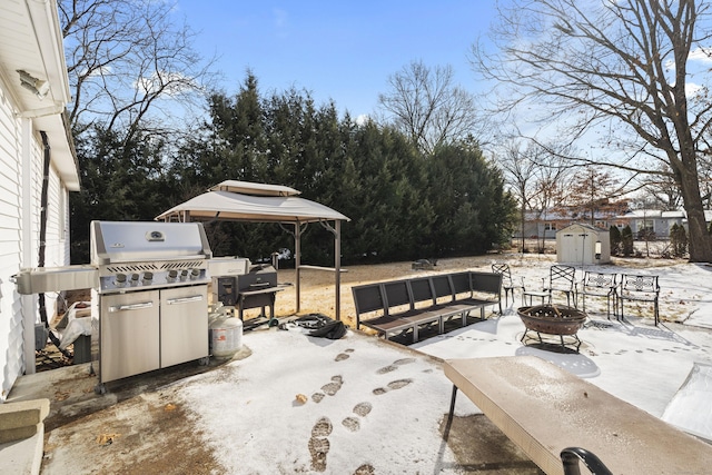 snow covered patio with a gazebo, an outdoor fire pit, and a storage unit