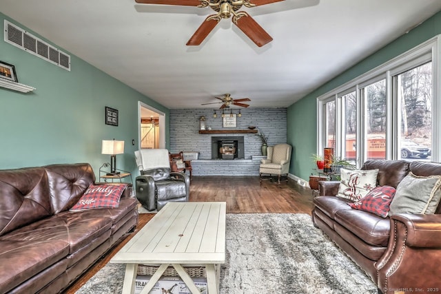 living room with hardwood / wood-style flooring, ceiling fan, brick wall, and a fireplace