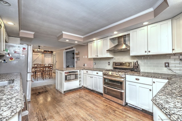 kitchen with wall chimney range hood, stainless steel appliances, light hardwood / wood-style floors, and white cabinets