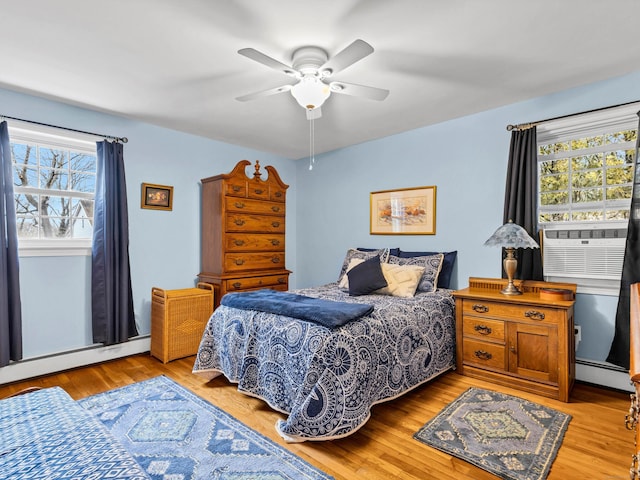 bedroom with baseboard heating, multiple windows, light wood finished floors, and a baseboard radiator