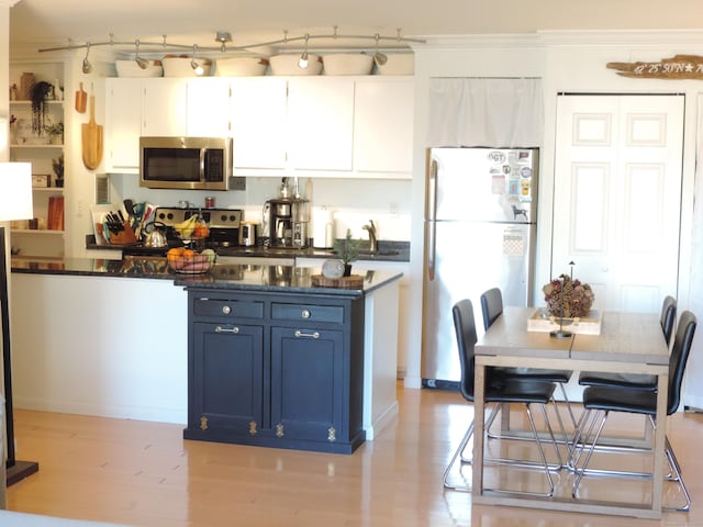 kitchen with appliances with stainless steel finishes, white cabinets, crown molding, blue cabinetry, and light wood-type flooring