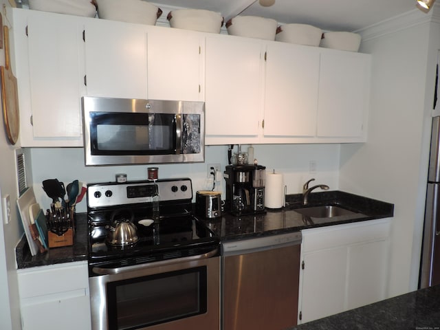 kitchen featuring sink, white cabinets, dark stone counters, stainless steel appliances, and crown molding