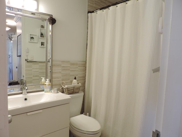 bathroom featuring walk in shower, vanity, toilet, and tile walls