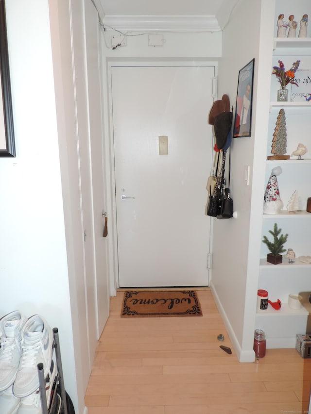 doorway with ornamental molding and light hardwood / wood-style floors