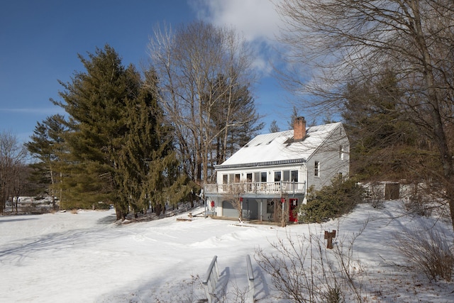 snow covered rear of property featuring a wooden deck and a garage