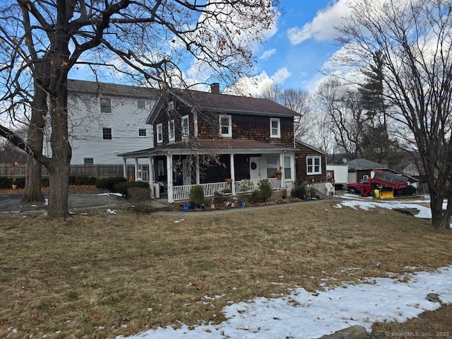 snow covered rear of property with a porch and a yard