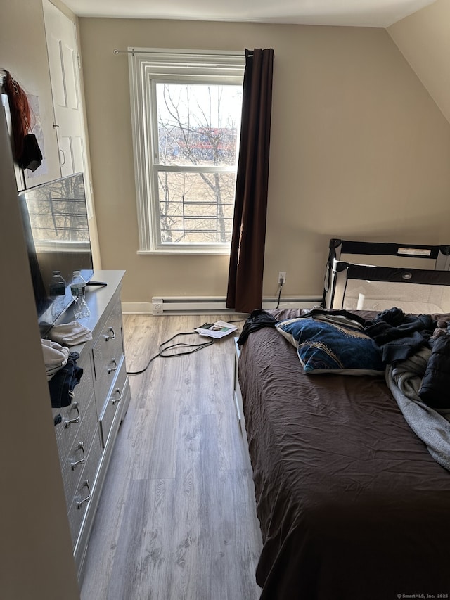 bedroom with vaulted ceiling, a baseboard heating unit, and light hardwood / wood-style floors