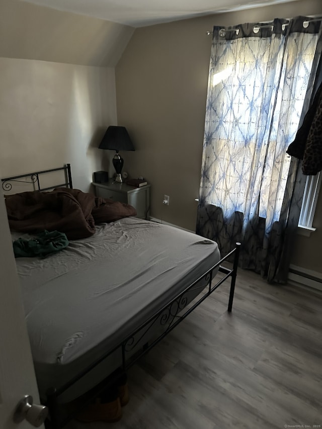 bedroom with a baseboard radiator, wood-type flooring, and vaulted ceiling