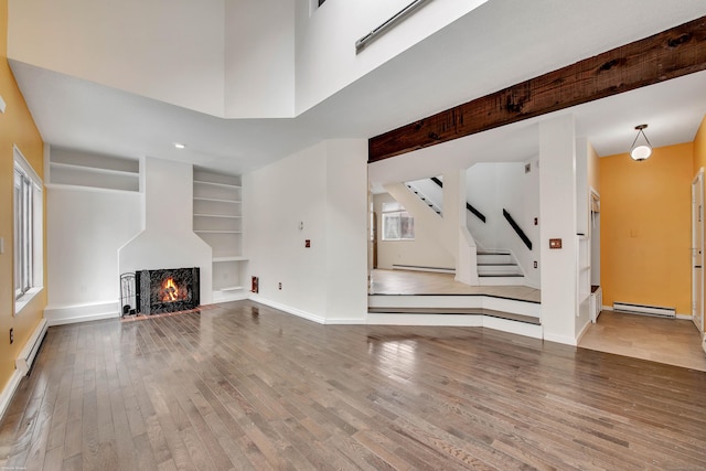 unfurnished living room featuring wood-type flooring, baseboards, and a baseboard heating unit