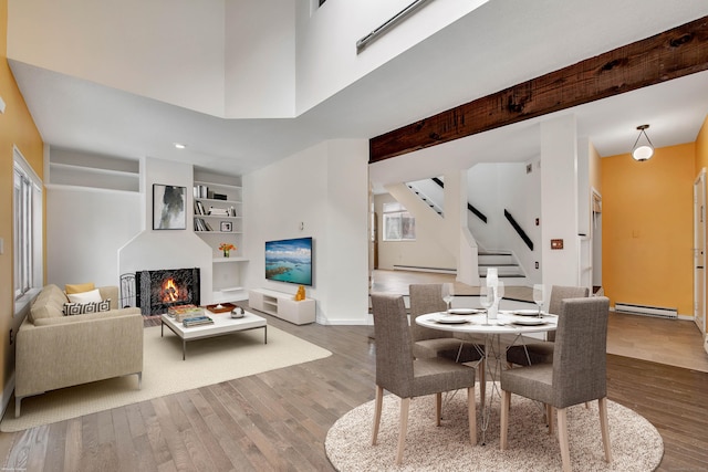 dining room with a warm lit fireplace, wood finished floors, baseboard heating, and stairway