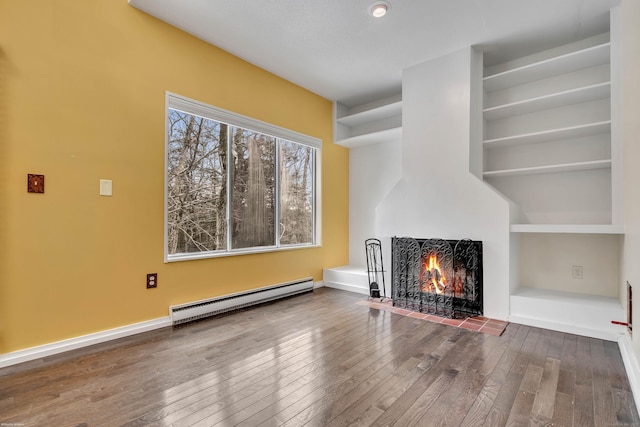 unfurnished living room featuring wood-type flooring, built in features, a baseboard heating unit, and a warm lit fireplace