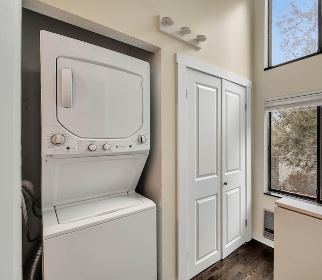 laundry room with dark wood-style flooring, stacked washer / drying machine, and laundry area
