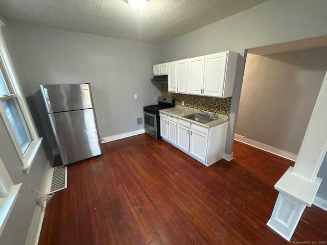 kitchen with appliances with stainless steel finishes, dark hardwood / wood-style floors, white cabinetry, decorative backsplash, and light stone counters