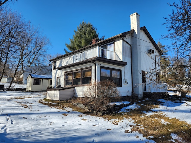 view of snowy exterior with a balcony and a shed