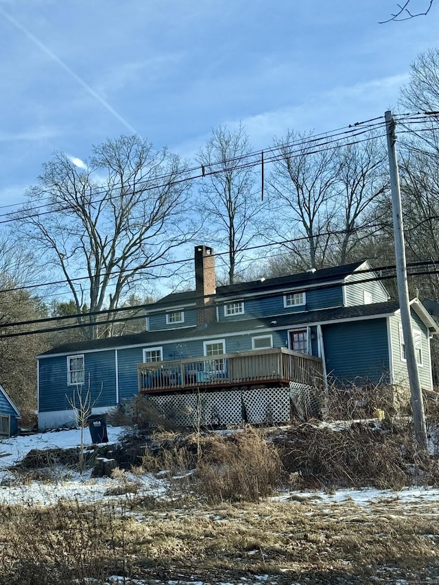 snow covered back of property with a deck and a chimney