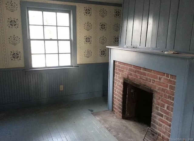 unfurnished living room featuring wainscoting, a brick fireplace, and wallpapered walls