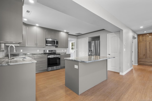 kitchen featuring sink, appliances with stainless steel finishes, gray cabinetry, a kitchen island, and light wood-type flooring