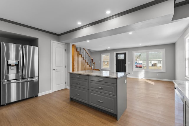 kitchen with gray cabinetry, light stone counters, crown molding, stainless steel fridge, and light hardwood / wood-style floors