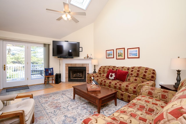 living room featuring a skylight, high vaulted ceiling, ceiling fan, a fireplace, and light hardwood / wood-style floors