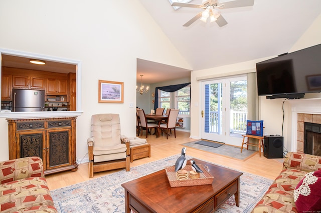 living room with high vaulted ceiling, ceiling fan with notable chandelier, a tile fireplace, and light wood-type flooring