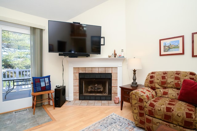 living room with light hardwood / wood-style flooring, a tiled fireplace, plenty of natural light, and lofted ceiling