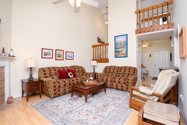 living room featuring a tiled fireplace, light hardwood / wood-style floors, ceiling fan, and a high ceiling