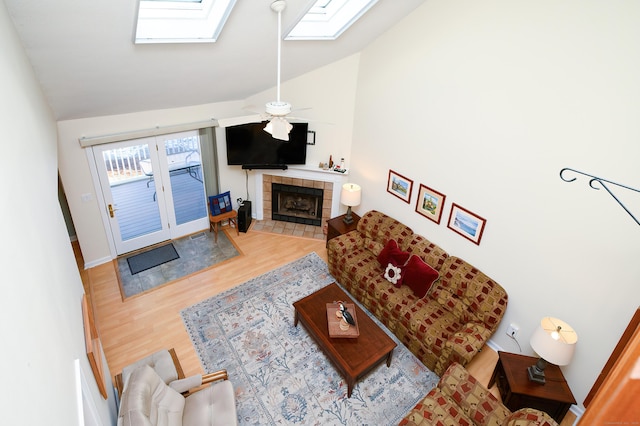 living room featuring ceiling fan, hardwood / wood-style flooring, a fireplace, and vaulted ceiling with skylight