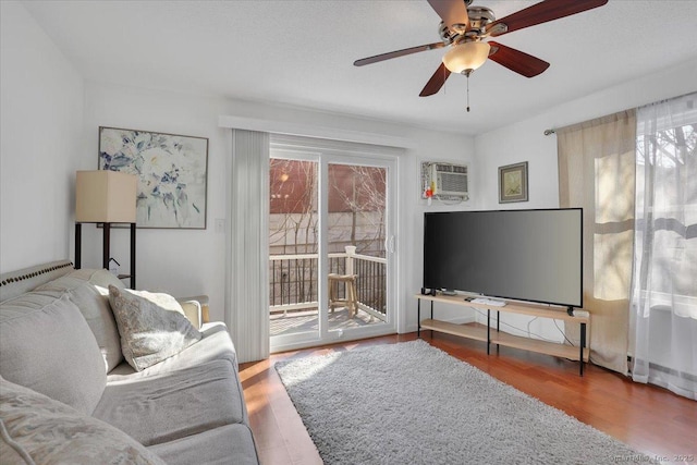 living room featuring wood-type flooring, ceiling fan, and a wall unit AC