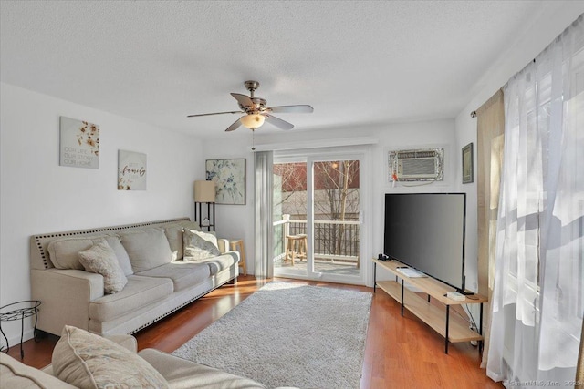 living room featuring hardwood / wood-style floors, a wall mounted air conditioner, a textured ceiling, and ceiling fan