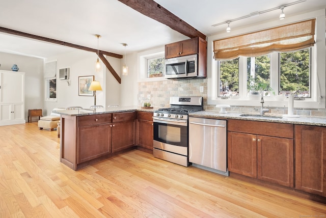 kitchen with sink, stainless steel appliances, light stone countertops, decorative light fixtures, and kitchen peninsula