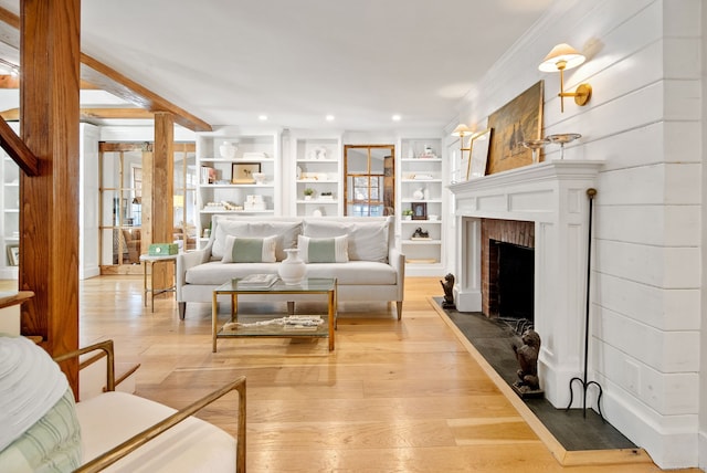 living room with a fireplace, built in features, light hardwood / wood-style floors, and ornamental molding