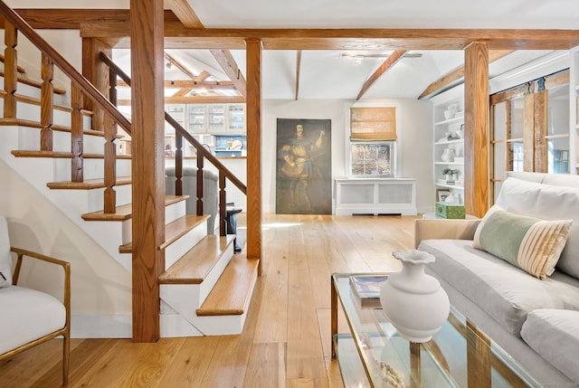 living room featuring radiator, vaulted ceiling with beams, light hardwood / wood-style flooring, ceiling fan, and built in shelves