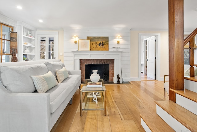 living room featuring built in shelves, ornamental molding, light hardwood / wood-style floors, and a brick fireplace